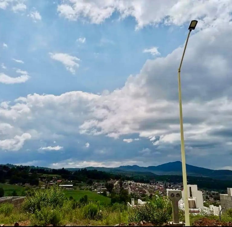 Panoramic landscape view of a rural village under a blue sky with white clouds and a tall street light.