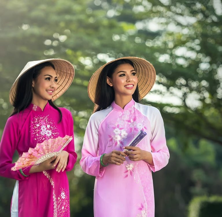 Zwei lächelnde Frauen in traditionellen vietnamesischen Ao Dai Kleidern mit kegelförmigen Strohhüten