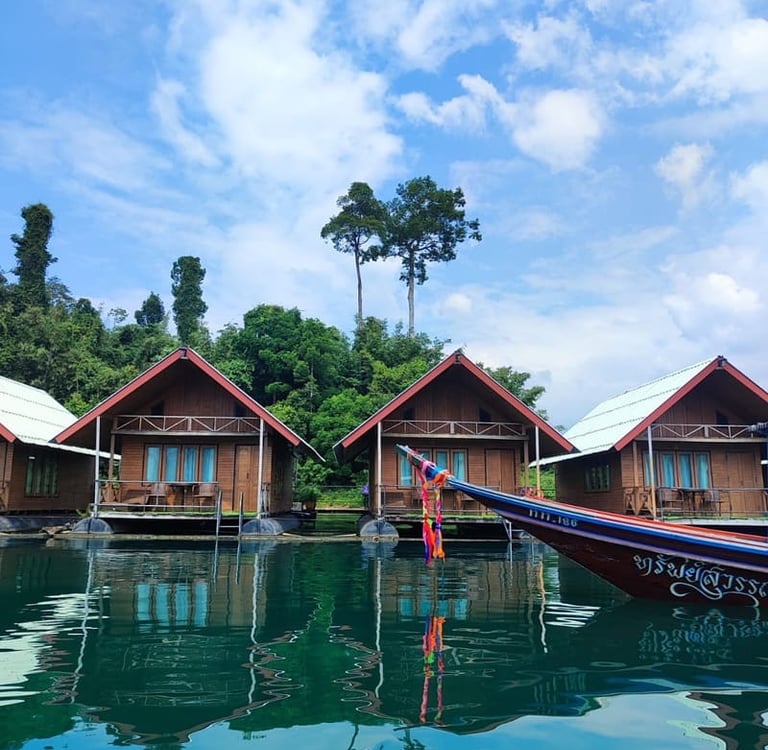 Schwimmende Holzbungalows auf dem Khao-Sok-See in Thailand mit einem traditionellen Longtail-Boot