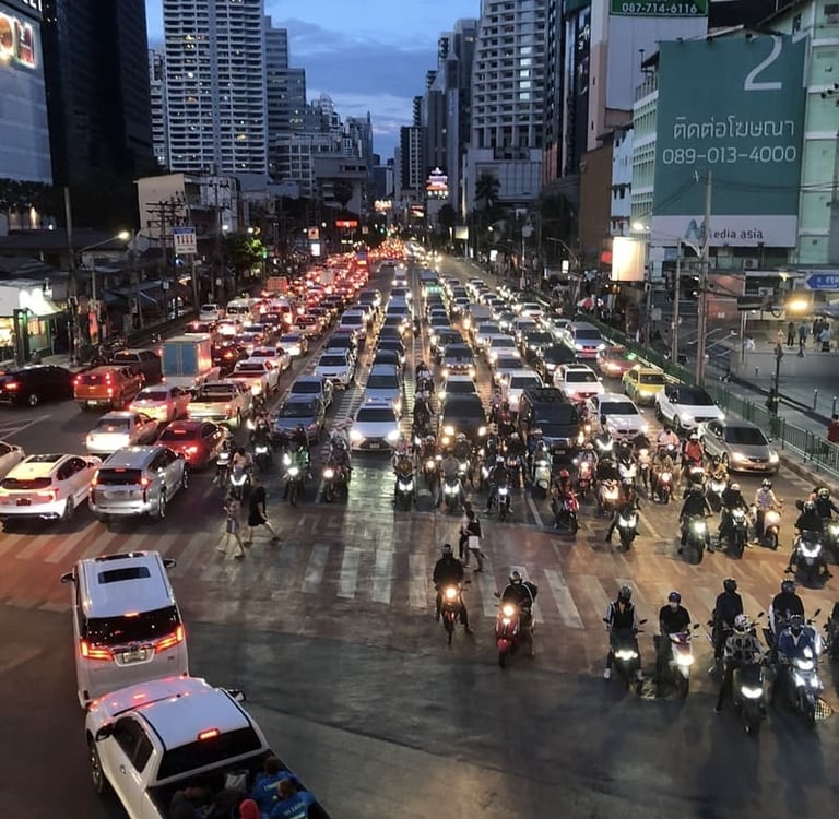 Starker Abendverkehr mit Autos und Motorrädern auf einer belebten Straße in Bangkok