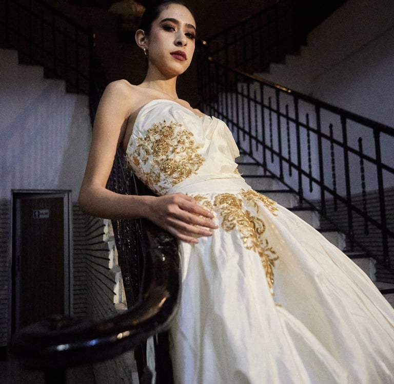 Elegant model in a white strapless gown with gold embroidery posing on a vintage staircase.