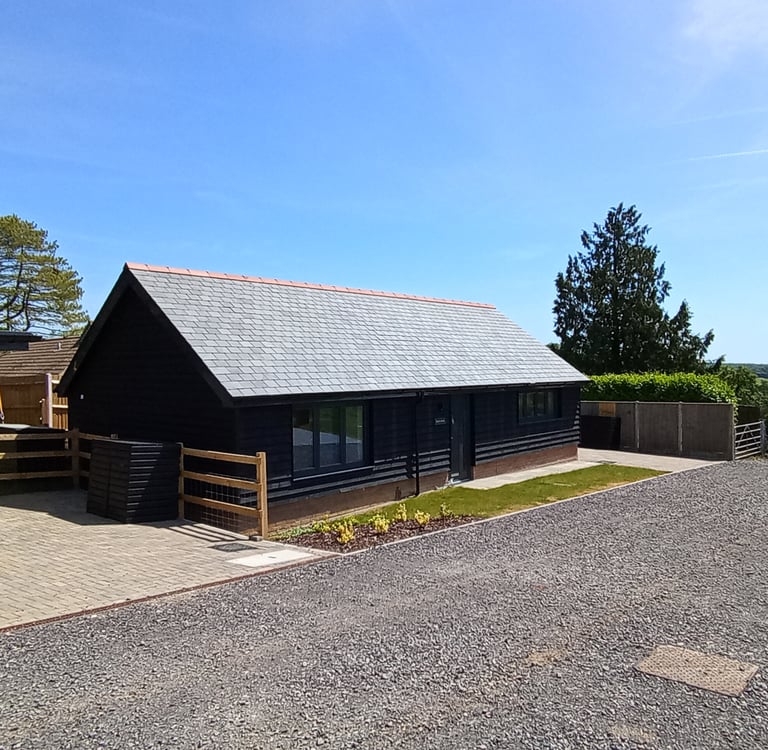 Modern black timber clad garden office with a grey slate roof next to a gravel driveway.