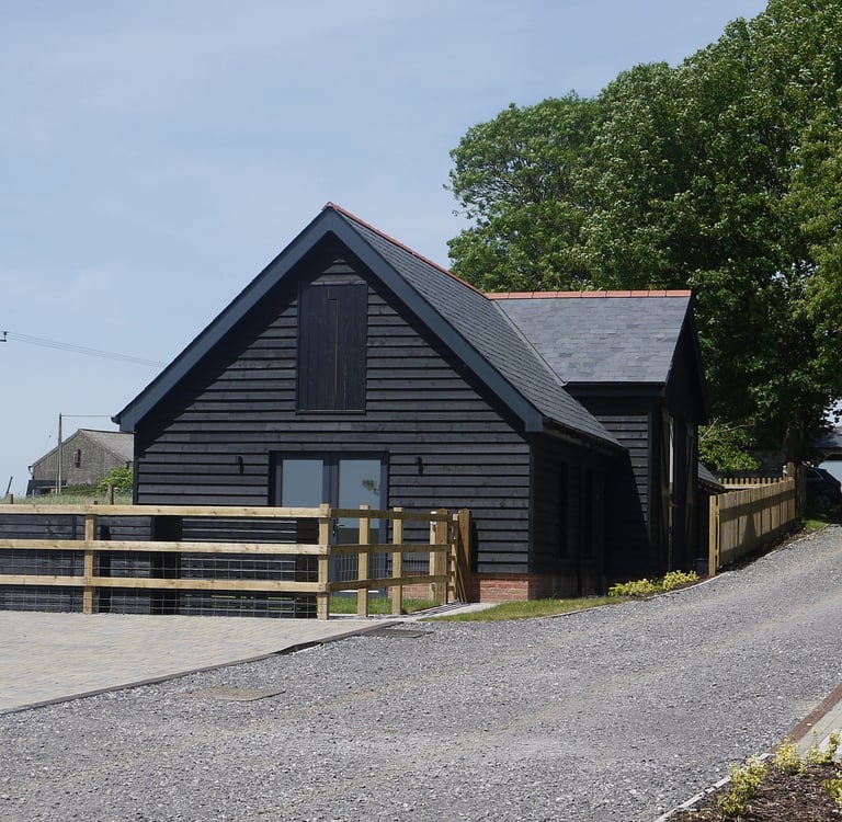A modern black timber-clad barn conversion with a slate roof and wooden post-and-rail fencing.