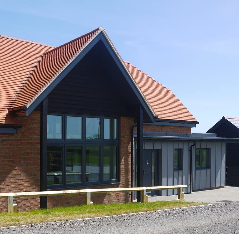 Modern red brick house with a black gabled roof, large windows, and grey zinc cladding extension.