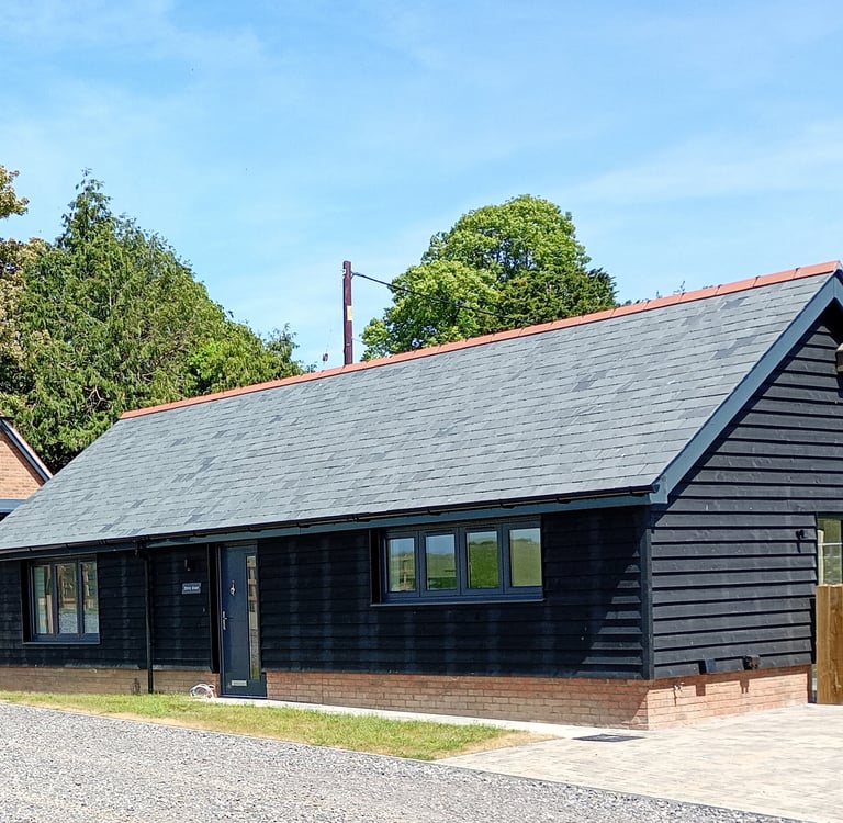Modern black timber barn conversion with slate roof and gravel driveway in a rural setting.