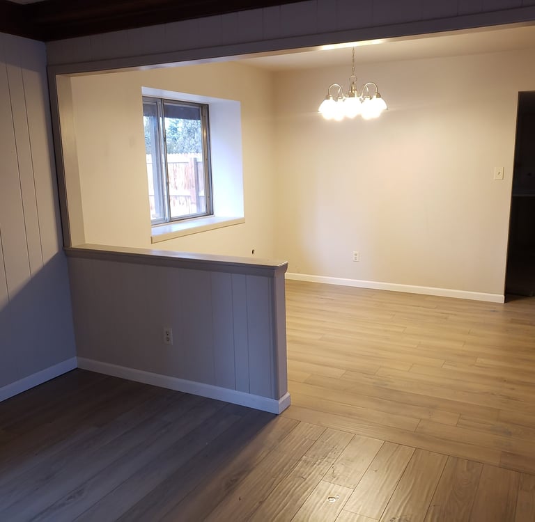 Newly renovated empty dining room with light oak laminate flooring and neutral grey paneled walls.