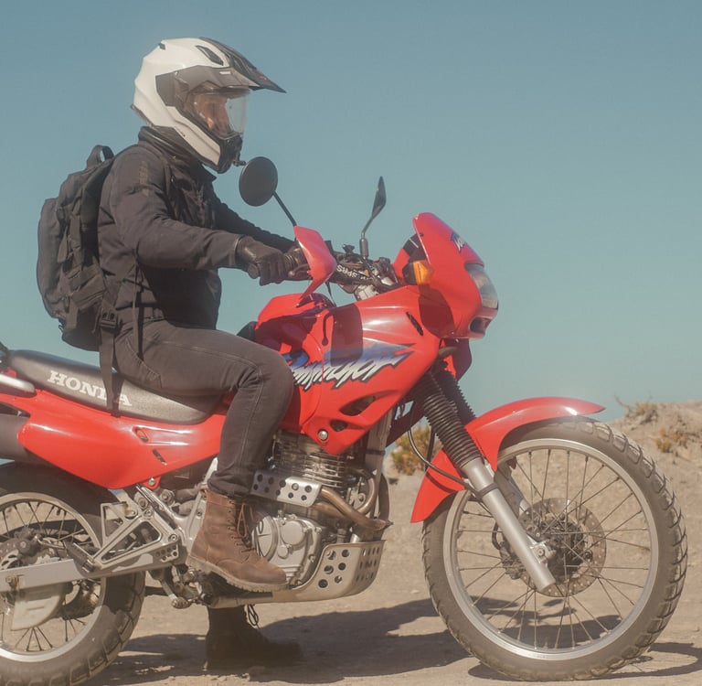 A man riding a Honda NX650 Dominator motorcycle out on a sandy surface