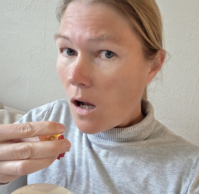 A blonde woman in a grey turtleneck holding a colorful gummy bear candy with a surprised facial expression.