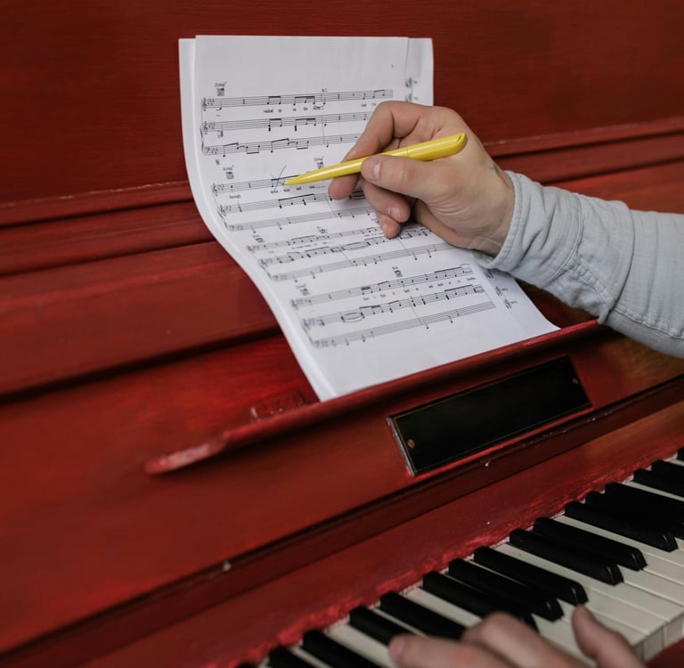 Musician composing music on a red piano while holding a yellow pen over sheet music.