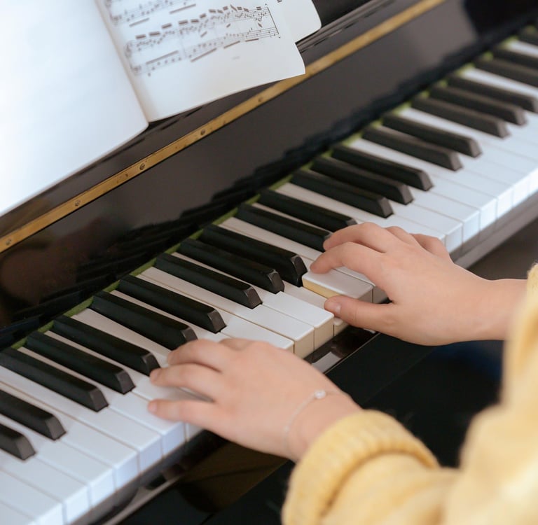 A student's hands playing classical music on a black upright piano with sheet music displayed.