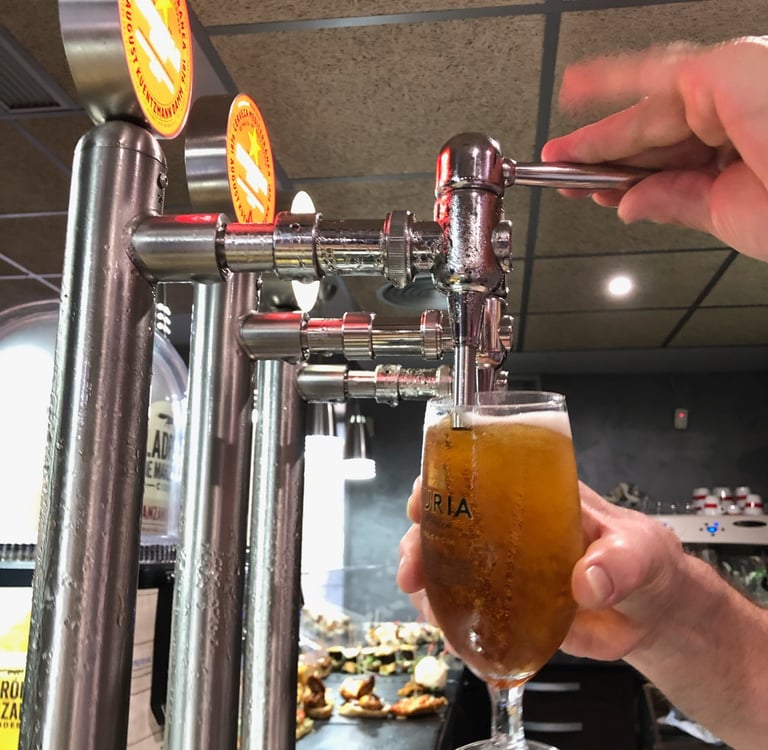 A bartender pouring a cold draft beer from a chrome tap into a glass at a Spanish tapas bar.