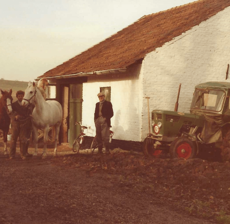 Historische foto van Hoeve Dinjens in Maastricht met een man, paarden en tractor voor de boerderij.