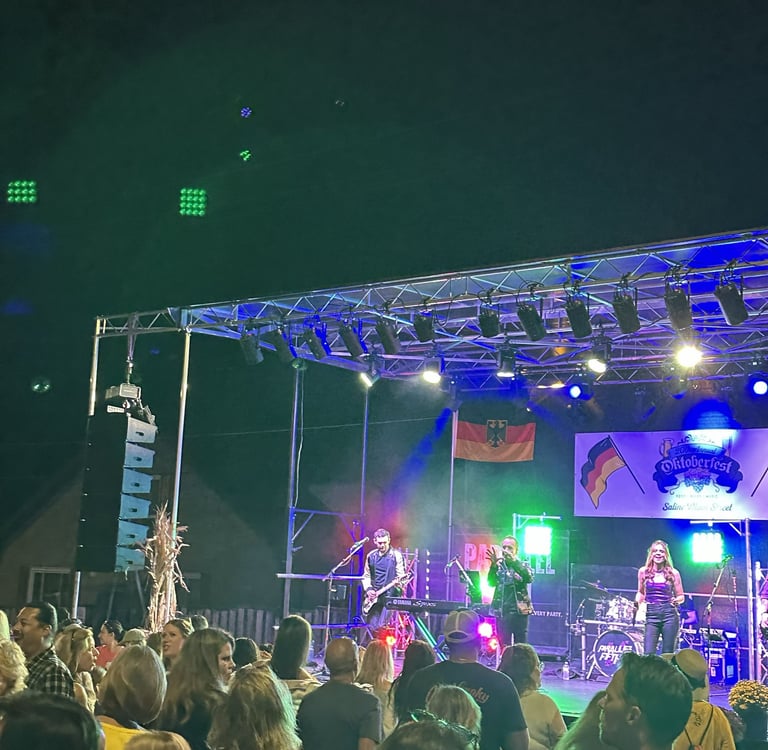 Live band performing on an outdoor stage at an Oktoberfest festival with a cheering crowd.