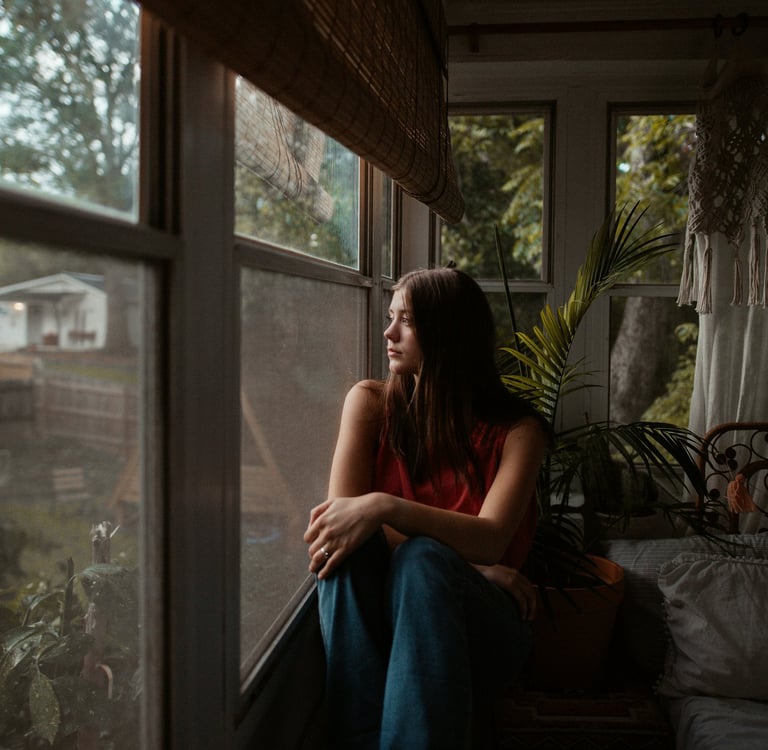 Woman sitting quietly at a window, looking tired — signs of burnout