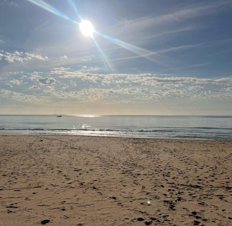 Peaceful morning by the Mediterranean Sea with a quiet beach, sparkling water, soft clouds and a small boat in the distance.