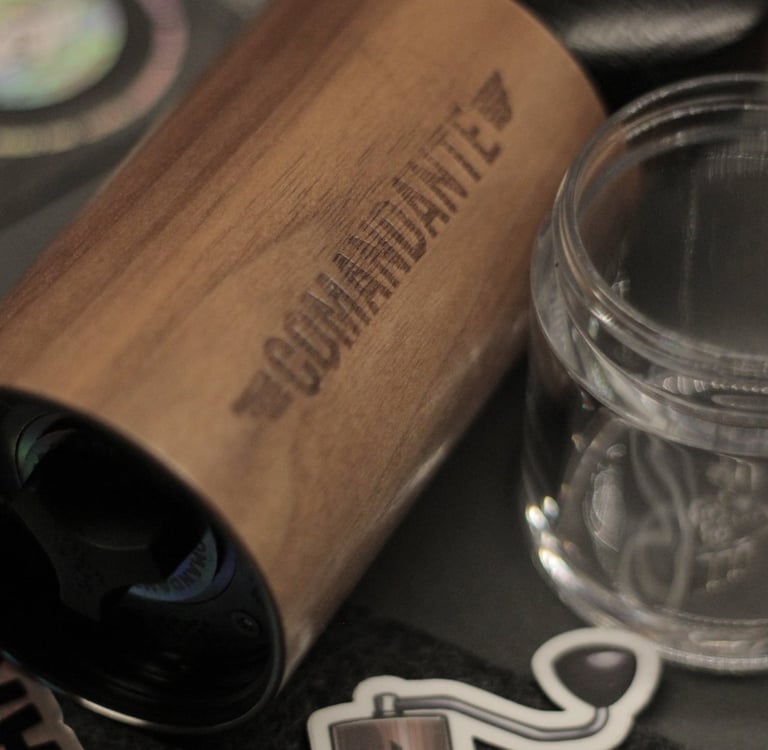 Comandante wood manual coffee grinder next to a glass jar and stickers for specialty coffee brewing.