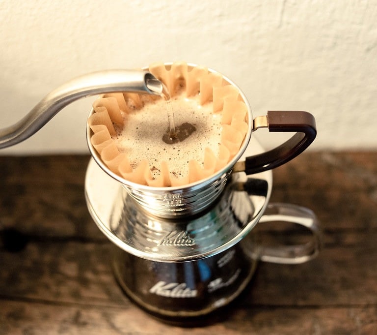Hot water pouring from a gooseneck kettle into a Kalita Wave dripper for pour over coffee.