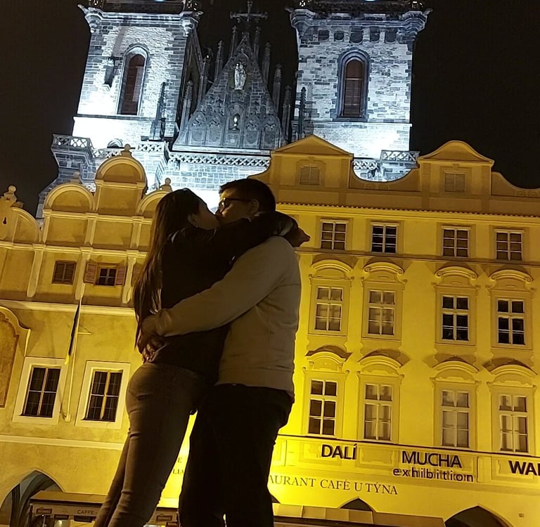 Pareja abrazándose frente a la Iglesia de Týn iluminada por la noche en Praga.
