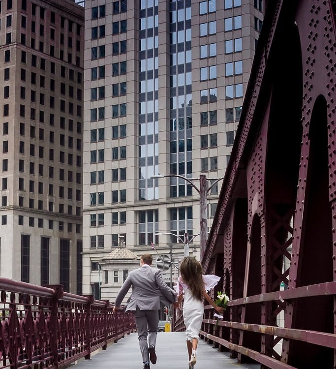 pareja de novios corriendo por puente de ciudad 