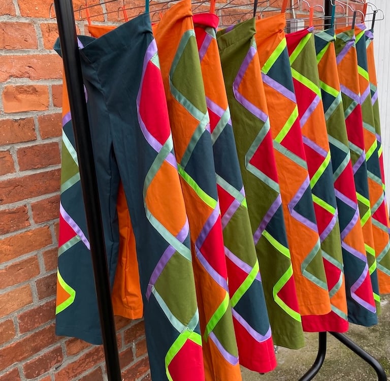 Handmade colorful patchwork trousers with geometric patterns hanging on a clothing rack.
