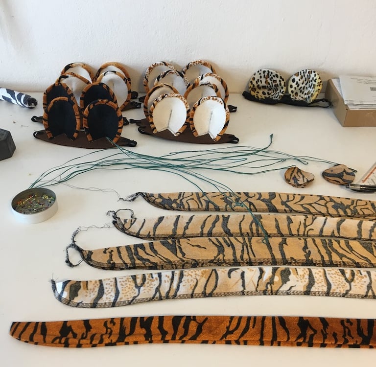 Handmade tiger and leopard animal ear headbands and tails on a white craft table.
