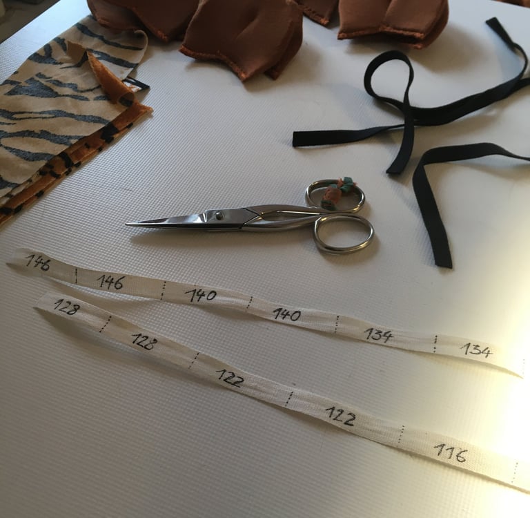 Sewing supplies including sharp scissors, size labels, tiger print fabric, and black elastic ribbon.
