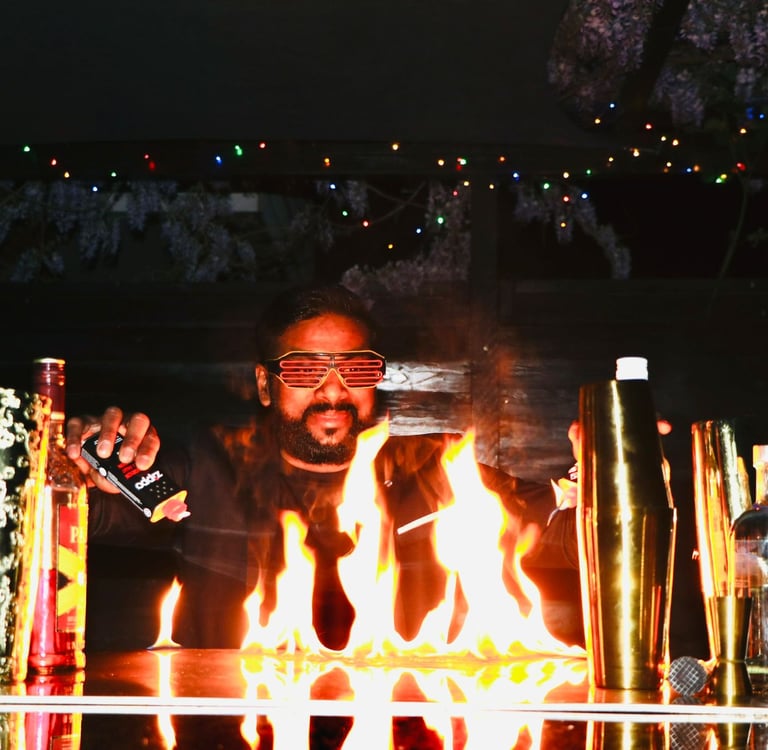 Professional mixologist performing a fire show with flames on a bar counter and cocktail shakers.