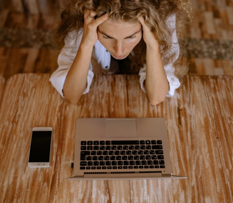 a woman sitting at a table with a laptop and a cell phone