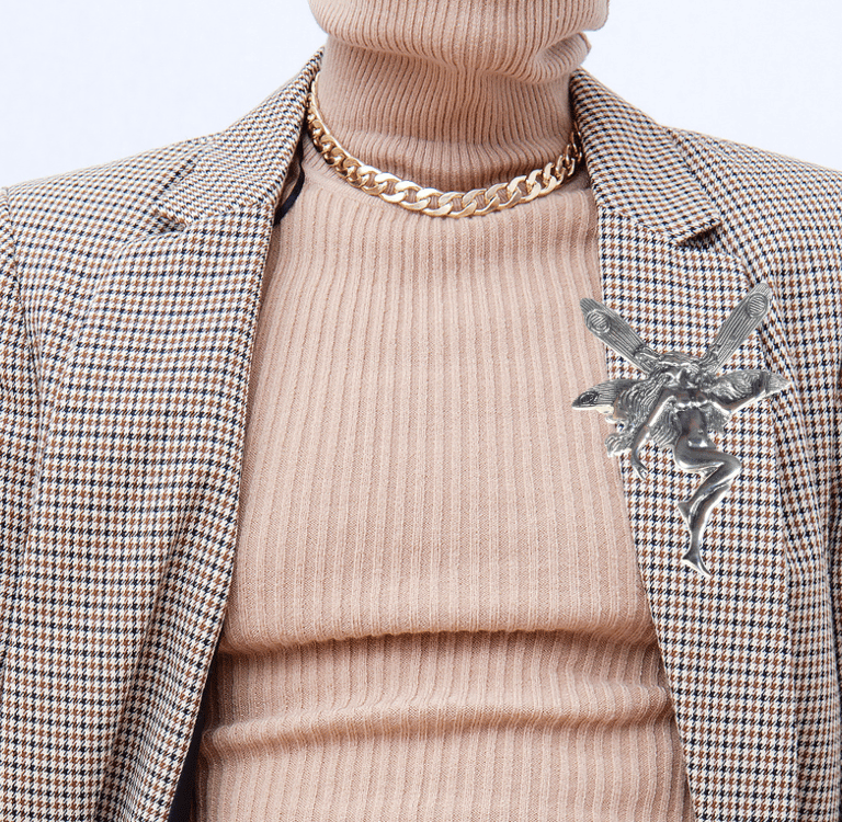 Vintage silver fairy brooch pinned to a brown plaid blazer with a beige turtle neck