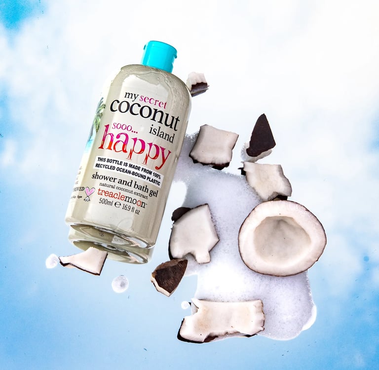 Treaclemoon Coconut Island shower gel surrounded by coconut pieces and foam on a cloudy blue sky