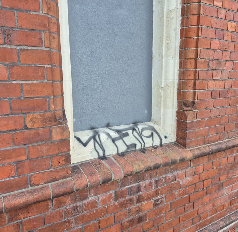 Black spray paint graffiti tag on the stone ledge of a red brick building window.