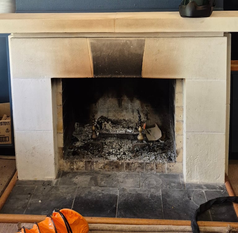 Traditional stone fireplace with soot stains and ashes on a black hearth.