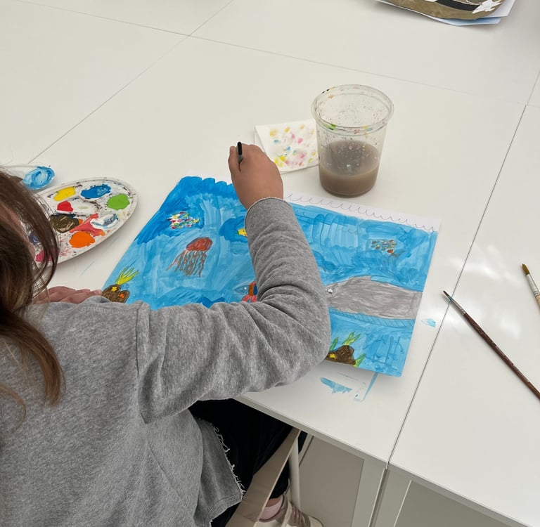 A kid painting a blue ocean scene with jellyfish and sharks in an art class.