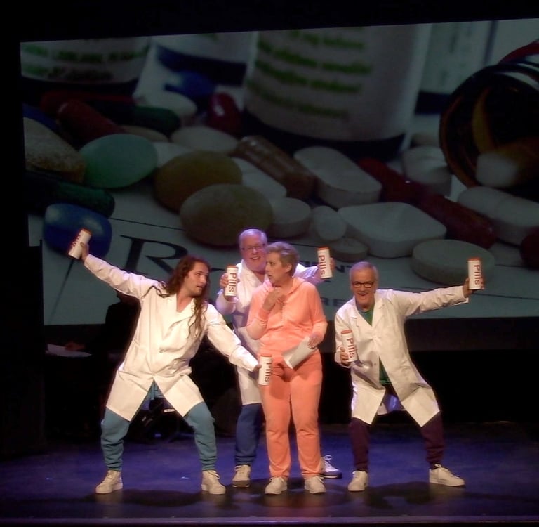 Performers in lab coats holding pill bottles dance in front of a pharmaceutical backdrop.