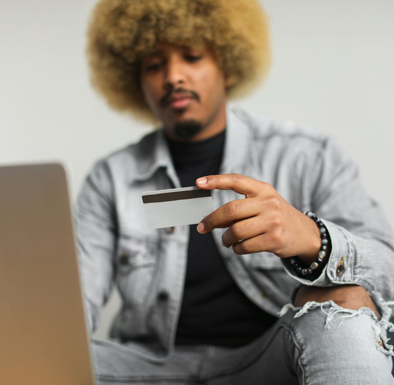 A man with an afro holds a credit card while using a laptop for secure online shopping and payments.