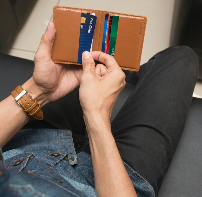 A man holding a slim brown leather bifold wallet with multiple credit cards and a Visa card.
