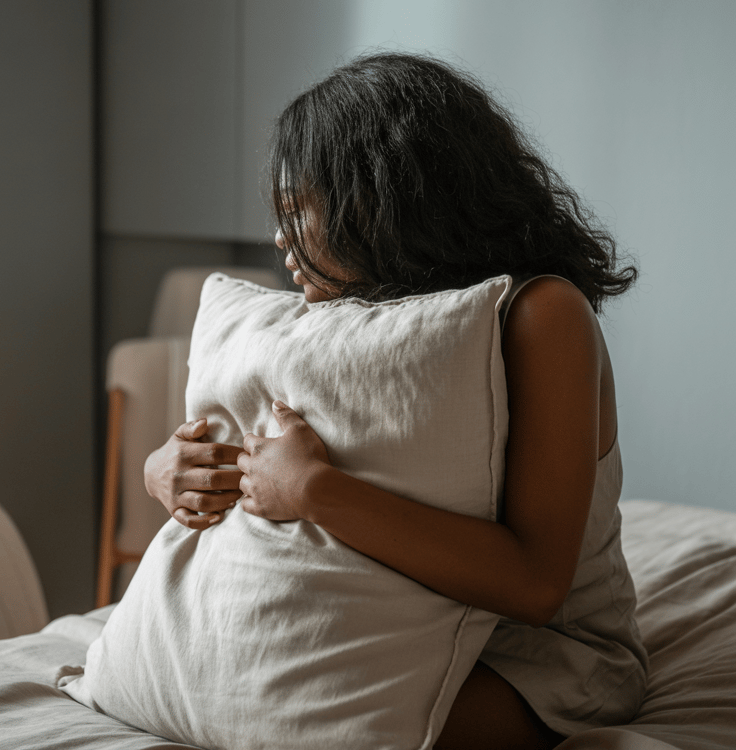une femme timide pensive sur son lit avec un coussin quel sert dans ses bras pour se réconforter.