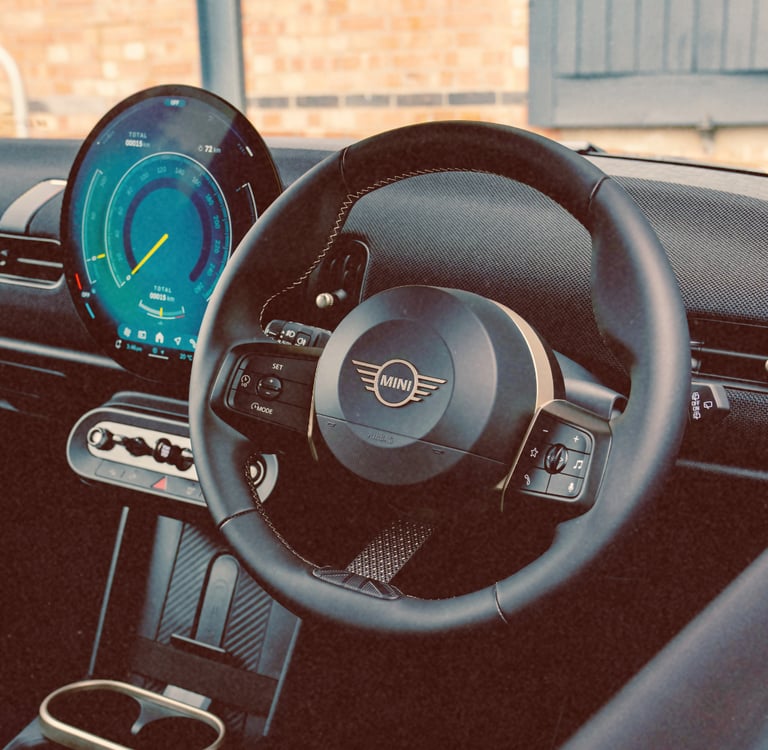 Modern interior of a Mini Cooper featuring a round digital dashboard and leather steering wheel.
