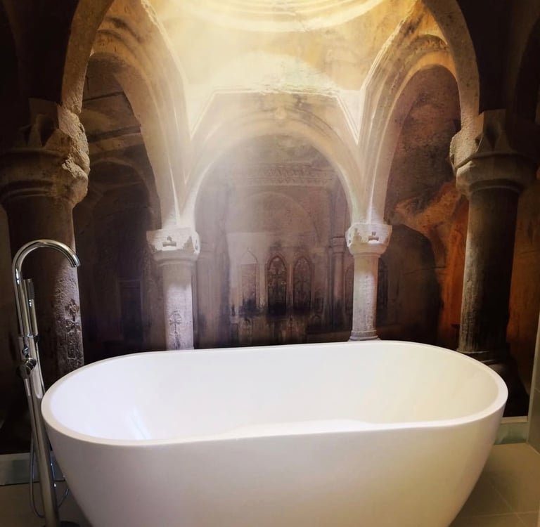 Modern white freestanding bathtub set against a mural of an ancient stone cathedral with sunlight.