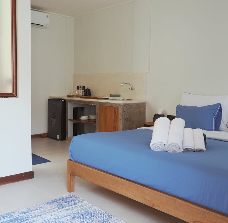 Modern hotel studio apartment featuring a queen bed with blue linens and a compact kitchenette.
