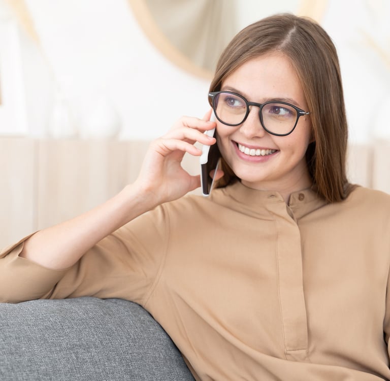 a woman in glasses and a brown shirt is talking on the phone