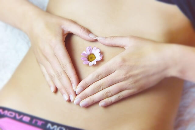 A woman's hands forming a heart shape over her stomach with a flower for gut health awareness.