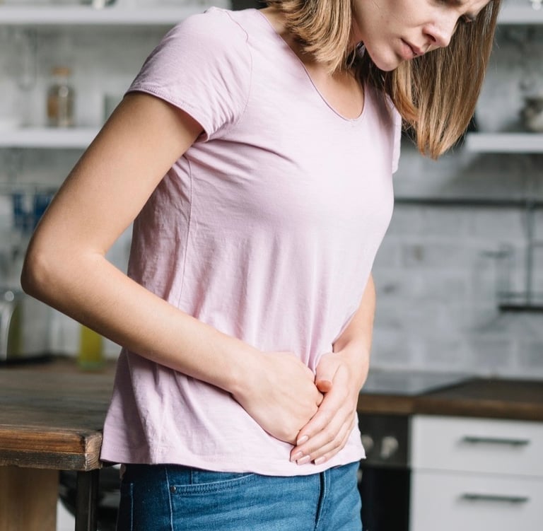 A young woman holding her stomach in pain due to digestive issues or menstrual cramps in a kitchen.