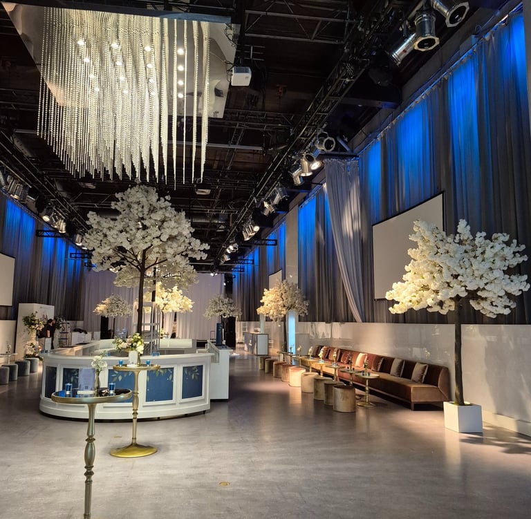 Luxury event venue featuring blue up lighting, white blossom décor, and a circular bar
