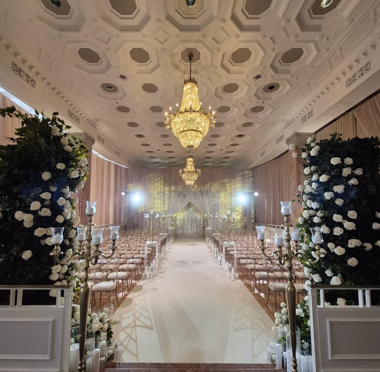 Elegant wedding ceremony setup in a grand ballroom with chandeliers, floral arches