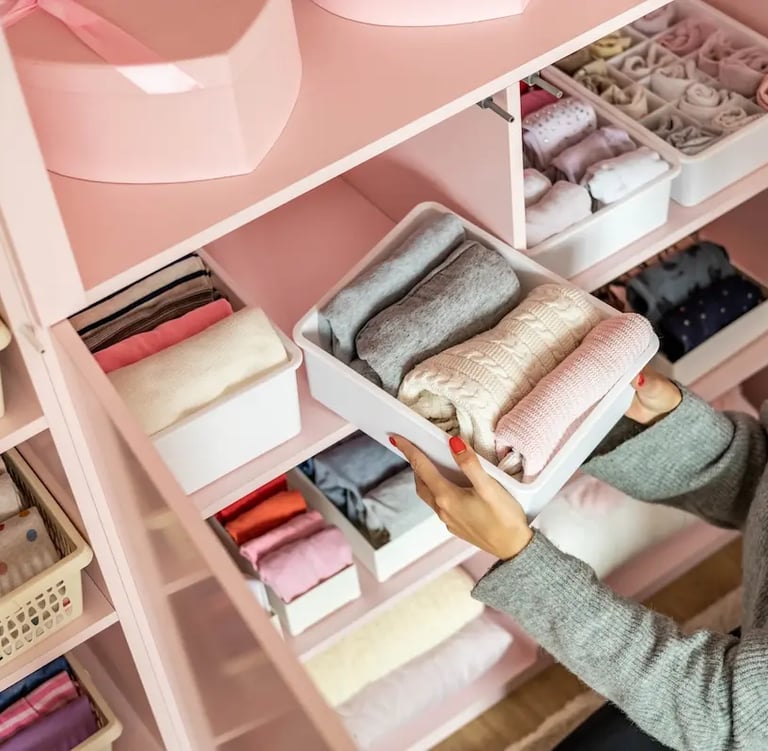 Woman organizing clothes in a pink closet using white storage bins for a tidy wardrobe.