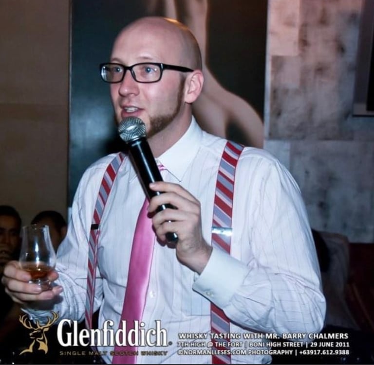 a man in shirt and tie presenting a whisky tasing with a microphone