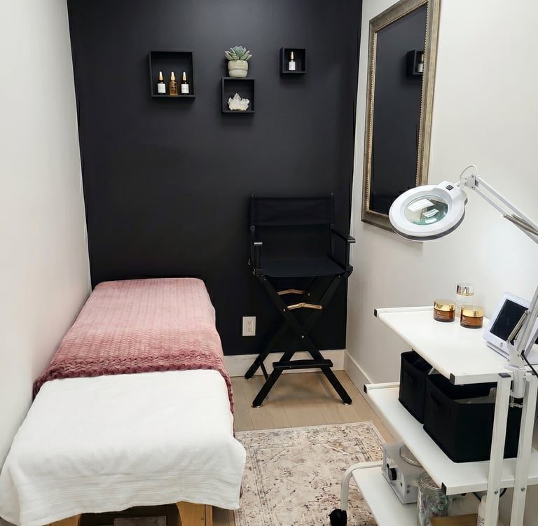 Modern aesthetician room with a facial treatment table, black accent wall, and professional skincare equipment.