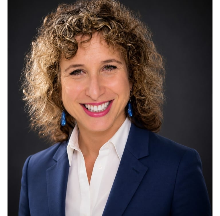 Professional headshot of a smiling woman with curly hair wearing a blue blazer and white shirt.