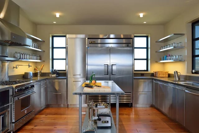 A modern home kitchen featuring a stainless steel table used as a central prep island with matching cabinetry and appliances.